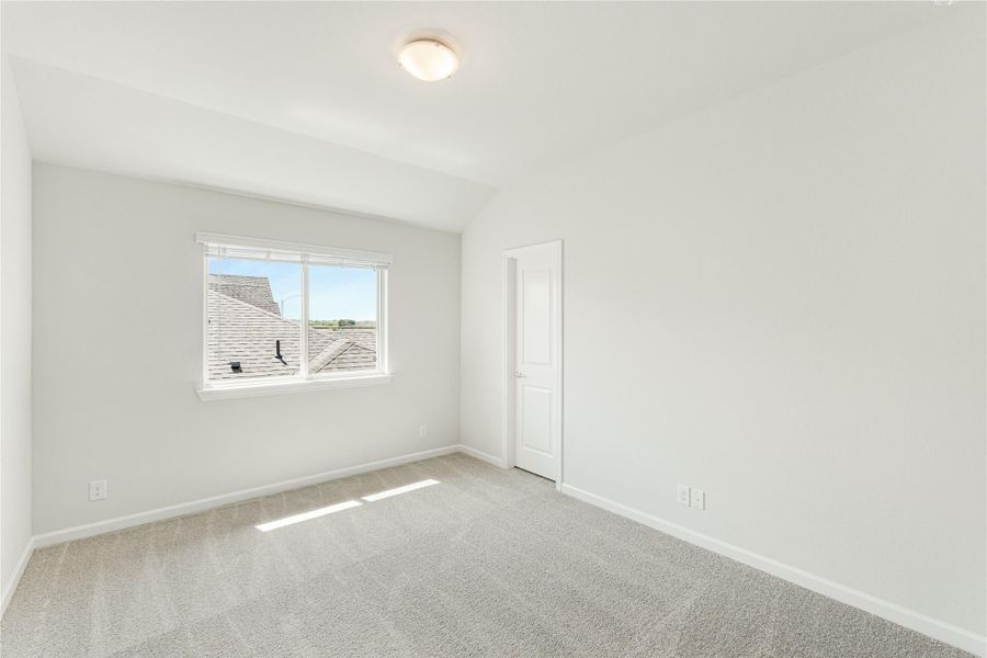 Empty bedroom with vaulted ceiling, carpet flooring, and a single window with natural light