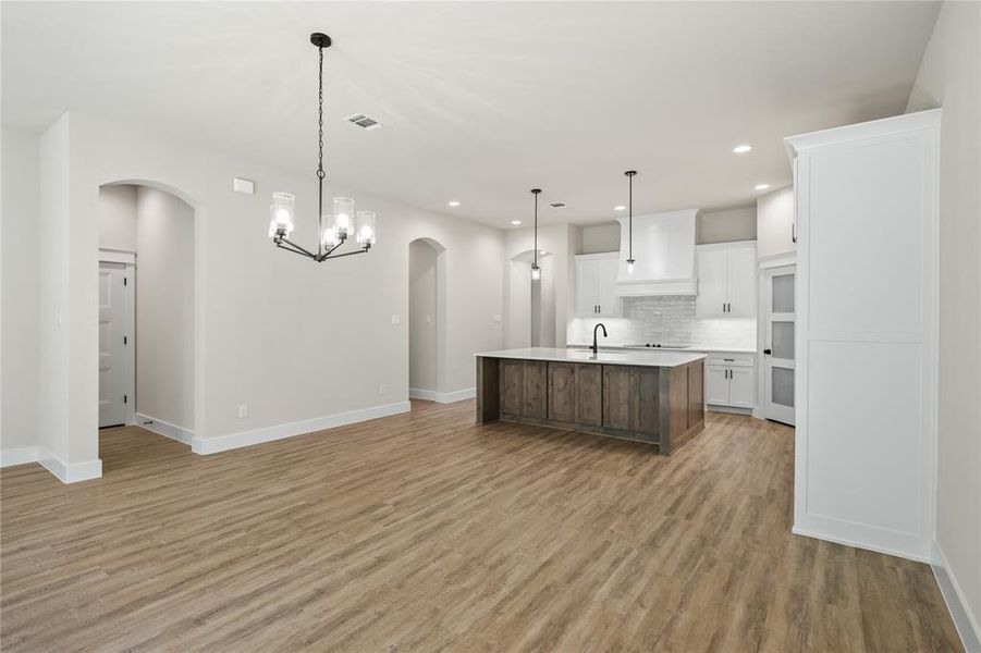 Dual tone kitchen with two tone color scheme, arched walkways, a kitchen island with sink, open floor plan, and hanging lights