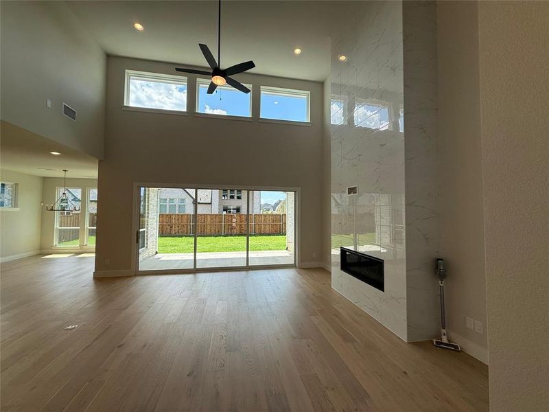 Unfurnished living room with a towering ceiling, a premium fireplace, wood finished floors, ceiling fan, and recessed lighting Unfurnished living room with a towering ceiling, a premium fireplace, wood finished floors, ceiling fan, and recessed lighting
