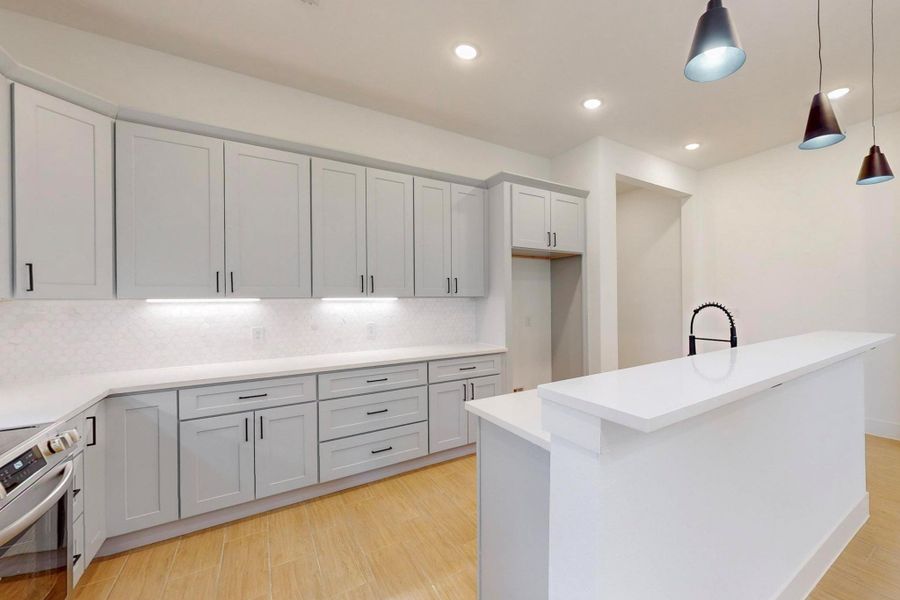 Kitchen featuring hanging light fixtures, electric stove, light wood finished floors, tasteful backsplash, and an island with sink
