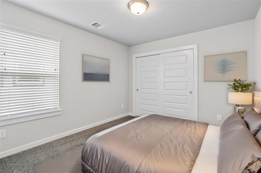 Secondary bedroom features plush carpet, neutral paint, lighting and a large window with privacy blinds.