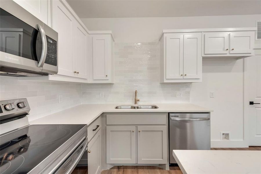 Kitchen featuring sink, white cabinets, backsplash, stainless steel appliances, and light hardwood / wood-style flooring