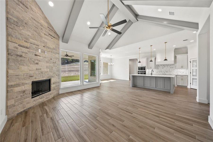 Unfurnished living room featuring a fireplace, beam ceiling, a chandelier, ceiling fan, and high vaulted ceiling