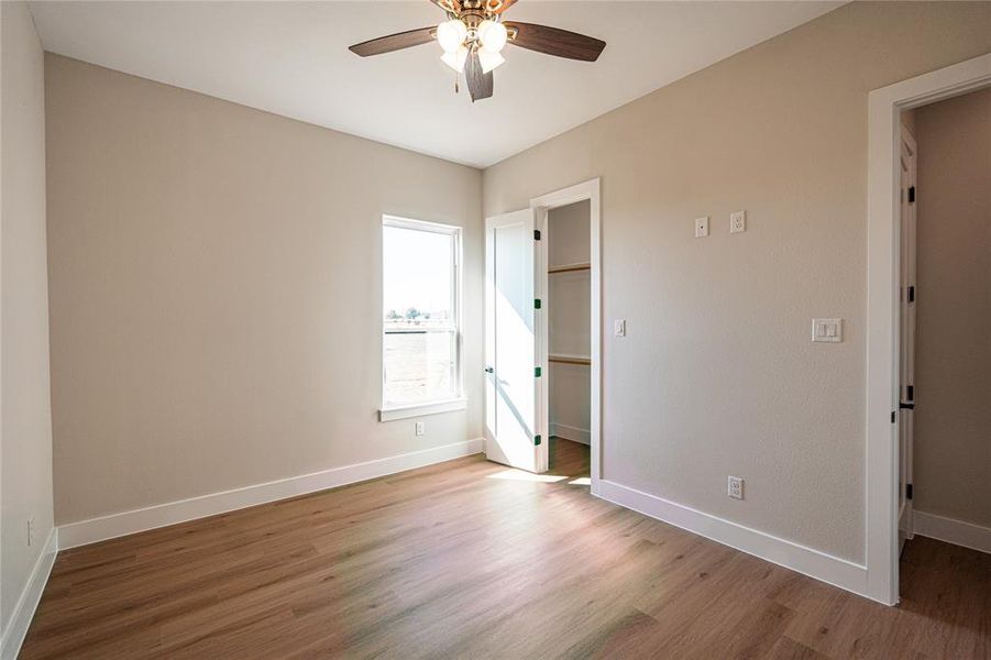 Unfurnished bedroom featuring a walk in closet, wood finished floors, and a ceiling fan