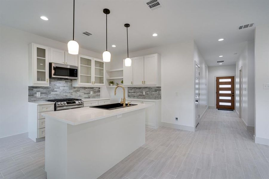 Kitchen featuring hanging light fixtures, a kitchen island with sink, tasteful backsplash, stainless steel appliances, and white cabinets