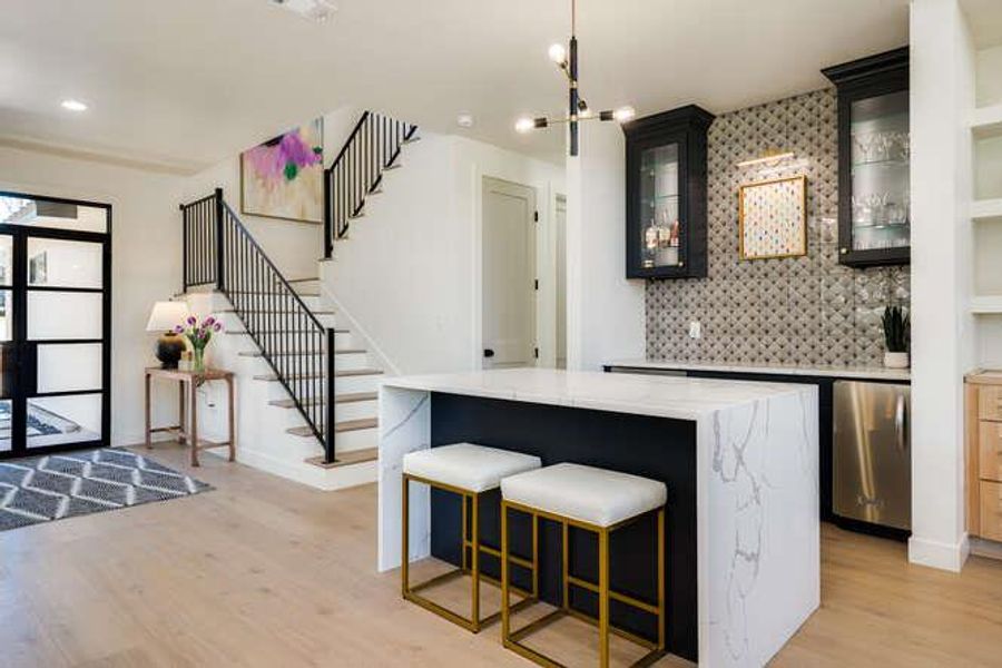 Indoor wet bar featuring stairway, tasteful backsplash, light wood-style flooring, glass insert cabinets, and light stone counters