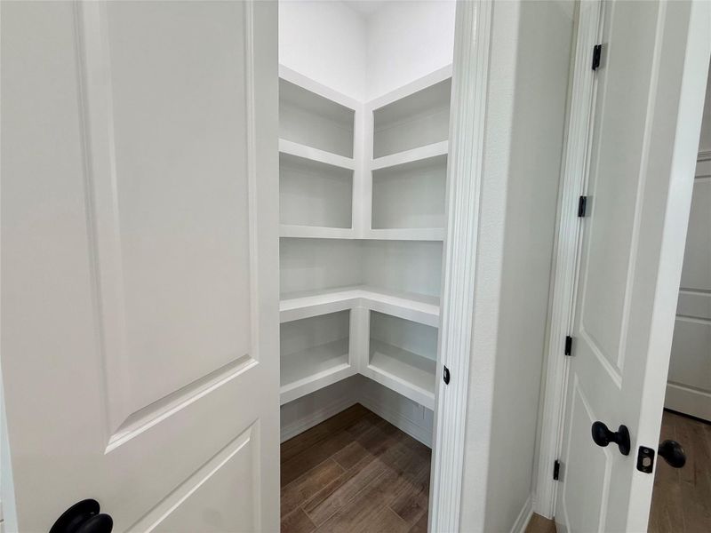 Walk-in pantry with extensive built-in shelving, white painted finishes, and wood-finish flooring