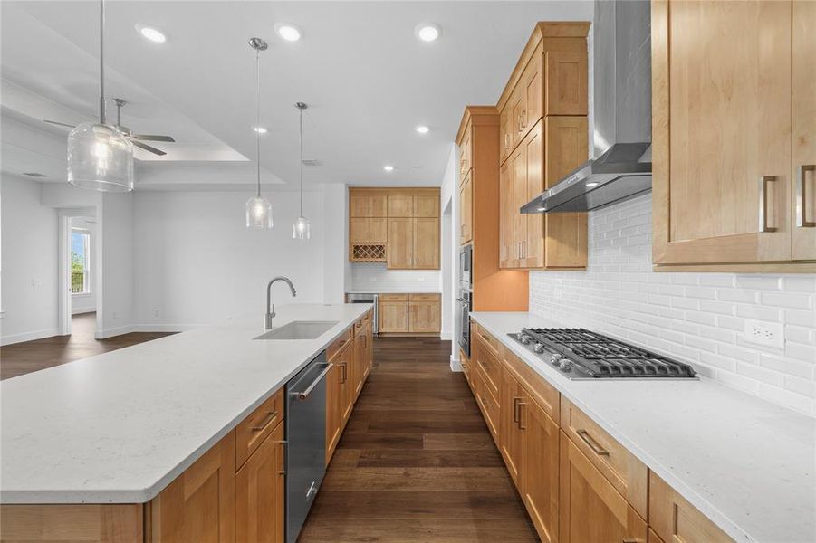 Spacious kitchen featuring light wood cabinetry, white countertops, a gas range with a stainless steel range hood, and an expansive island with an integrated sink and pendant lighting