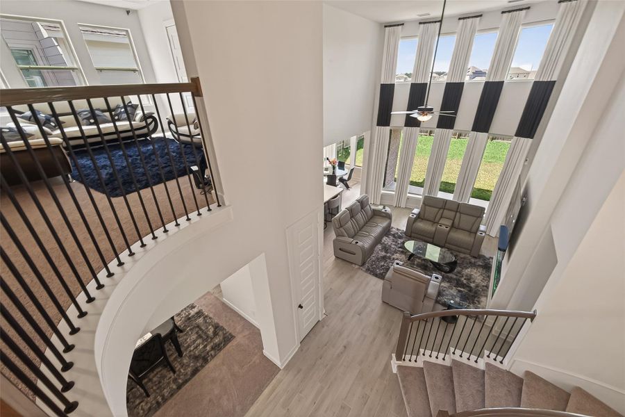 This photo showcases a modern, open-concept living space with high ceilings and large windows, providing abundant natural light. The room features a cozy seating area with stylish furniture, a view of the lush backyard, and a staircase leading to a loft or upper level.