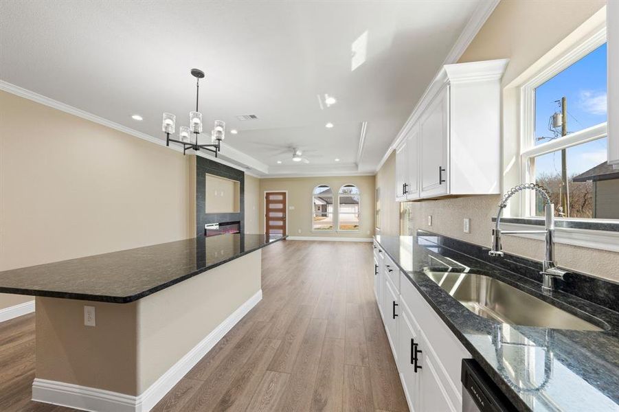 Kitchen with wood finished floors, a sink, baseboards, white cabinets, and a raised ceiling