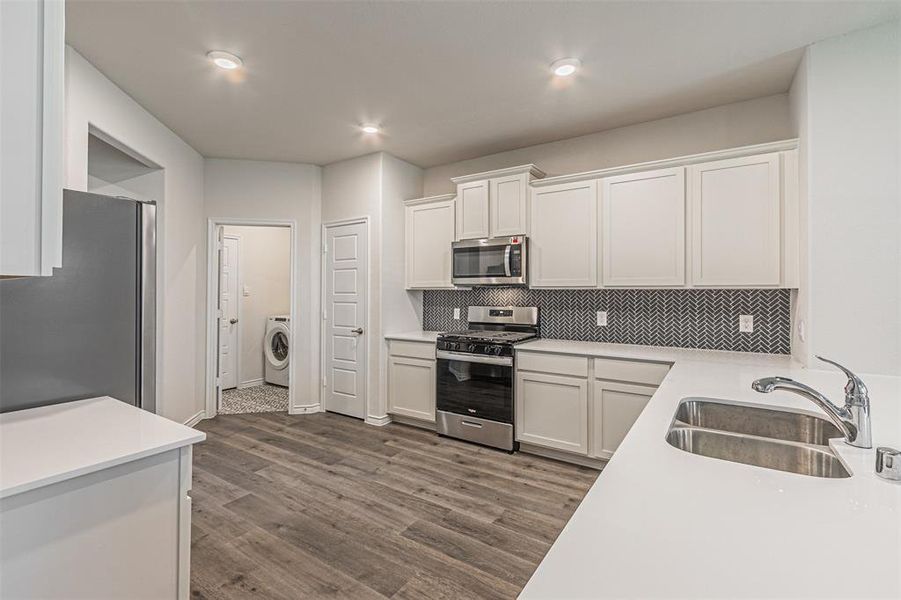 Kitchen with washer / dryer, sink, appliances with stainless steel finishes, and white cabinetry