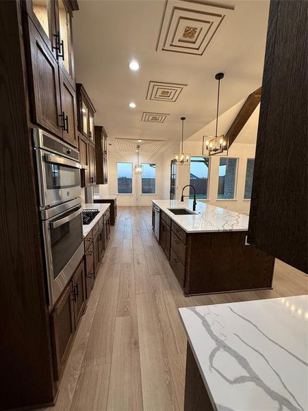 Kitchen with dark brown cabinets, glass insert cabinets, light wood-type flooring, pendant lighting, and light stone counters Kitchen with dark brown cabinets, glass insert cabinets, light wood-type flooring, pendant lighting, and light stone counters