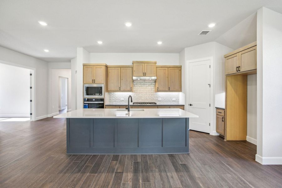 Kitchen featuring recessed lighting, a kitchen island with sink, tasteful backsplash, dark wood-style floors, and appliances with stainless steel finishes Kitchen featuring recessed lighting, a kitchen island with sink, tasteful backsplash, dark wood-style floors, and appliances with stainless steel finishes