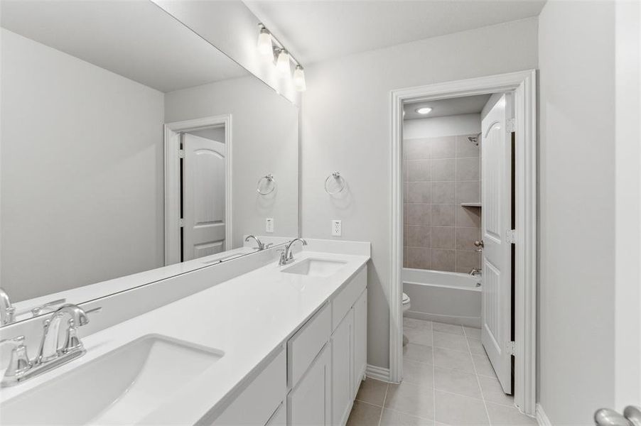 Bathroom featuring double vanity, light tile patterned floors, and washtub / shower combination