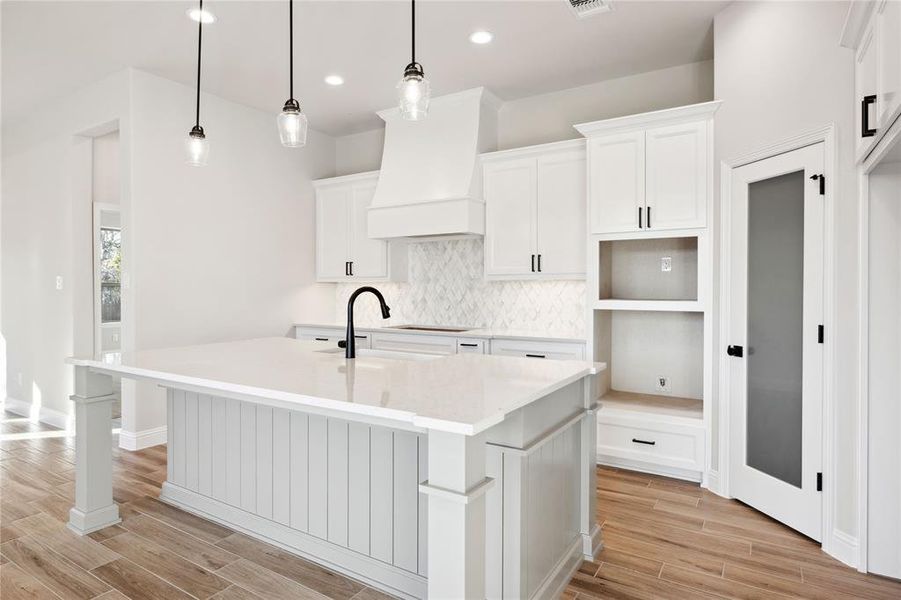 Kitchen with pendant lighting, white cabinets, a center island with sink, and premium range hood