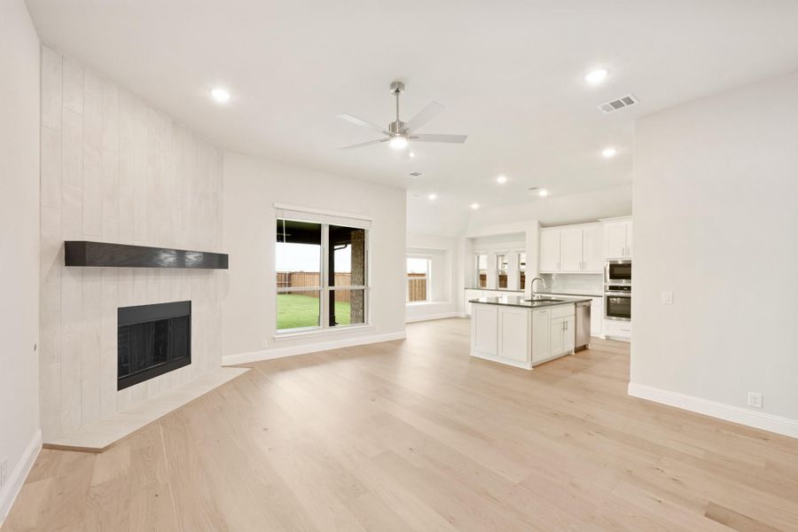 Open living area with shiplap fireplace, hardwood floors, and open-concept kitchen with white island in background