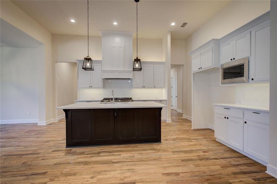 Kitchen has custom cabinets, large island with breakfast bar, tile backsplash and stone counters.