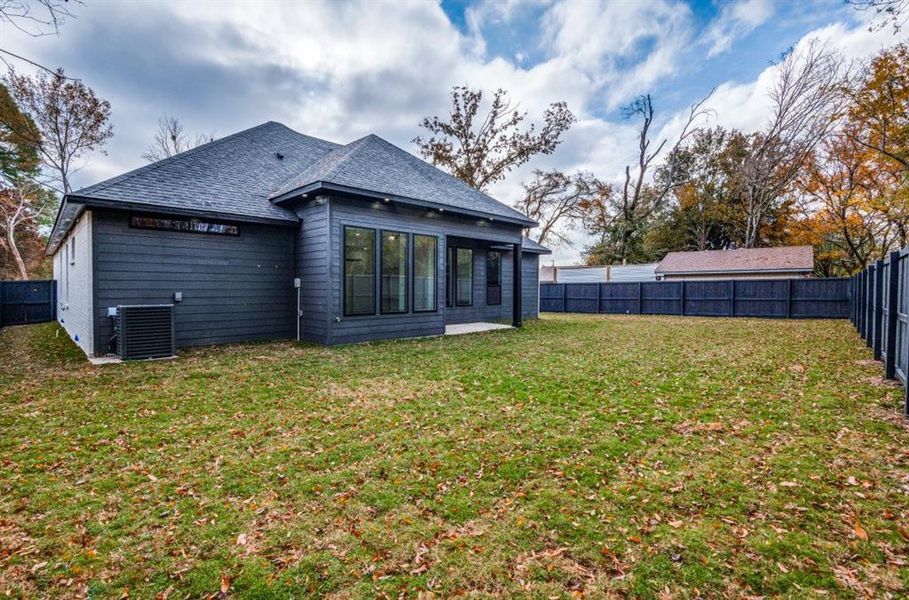 Back of property with central AC unit and a lawn