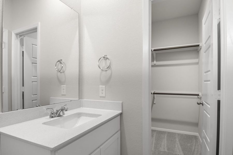A bathroom with white vanity with white countertops, a mirror, and a walk-in closet.