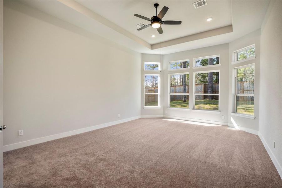 This spacious primary bedroom, where serene vibes meet natural light through oversized windows. The neutral palette and plush carpeting create a cozy atmosphere, complementing the high ceilings and sleek fan.