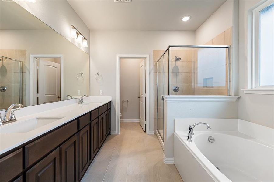 Full bath featuring double vanity, a shower stall, a bath, and light tile patterned flooring