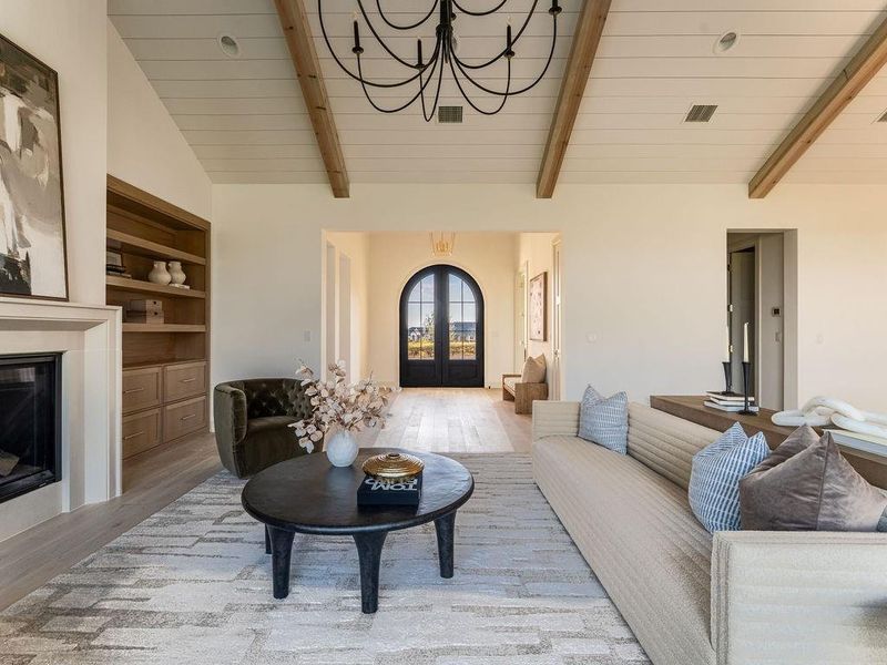 Living room with light wood-type flooring, a glass covered fireplace, french doors, and a chandelier