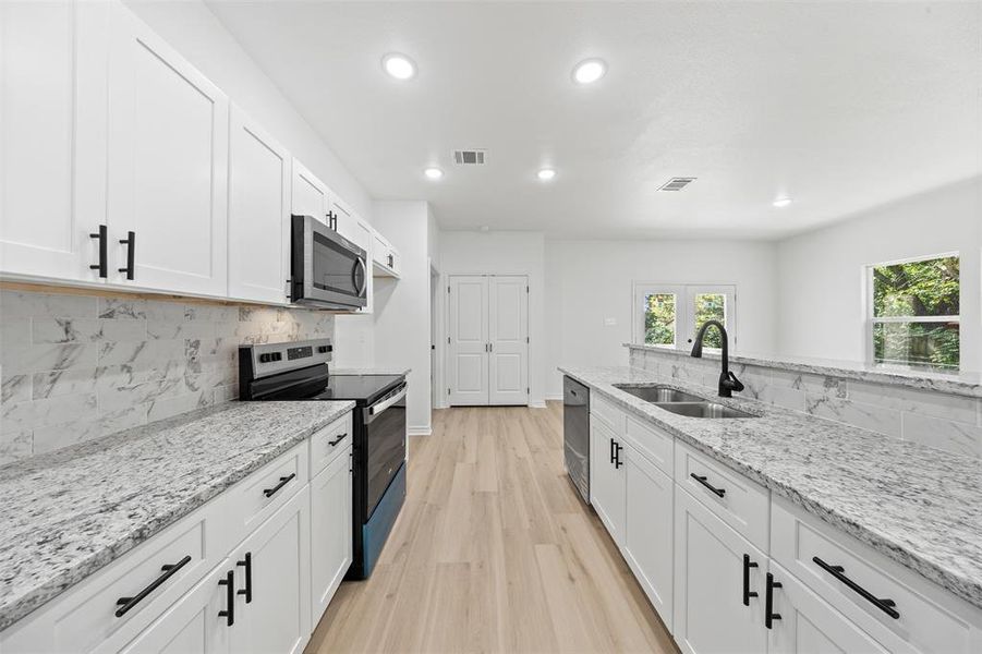 Kitchen featuring light stone countertops, appliances with stainless steel finishes, white cabinets, backsplash, and recessed lighting