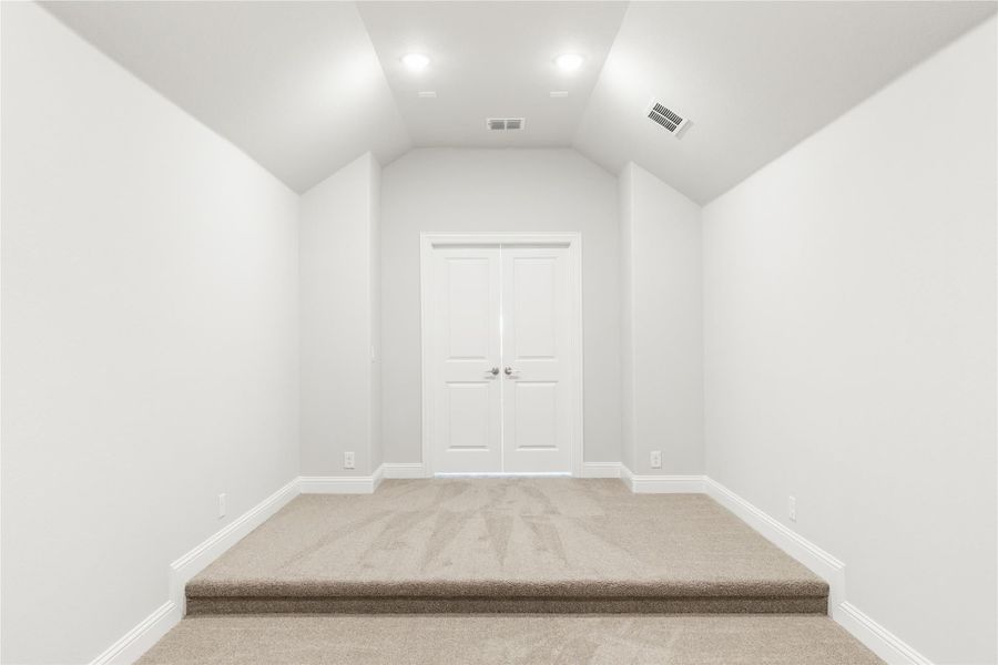 Empty room with vaulted ceiling, beige carpet, raised platform, and white double doors Empty room with vaulted ceiling, beige carpet, raised platform, and white double doors