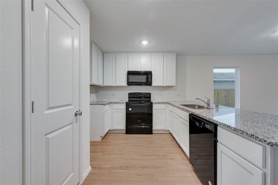 Kitchen featuring light wood-type flooring, light stone counters, sink, black appliances, and white cabinetry