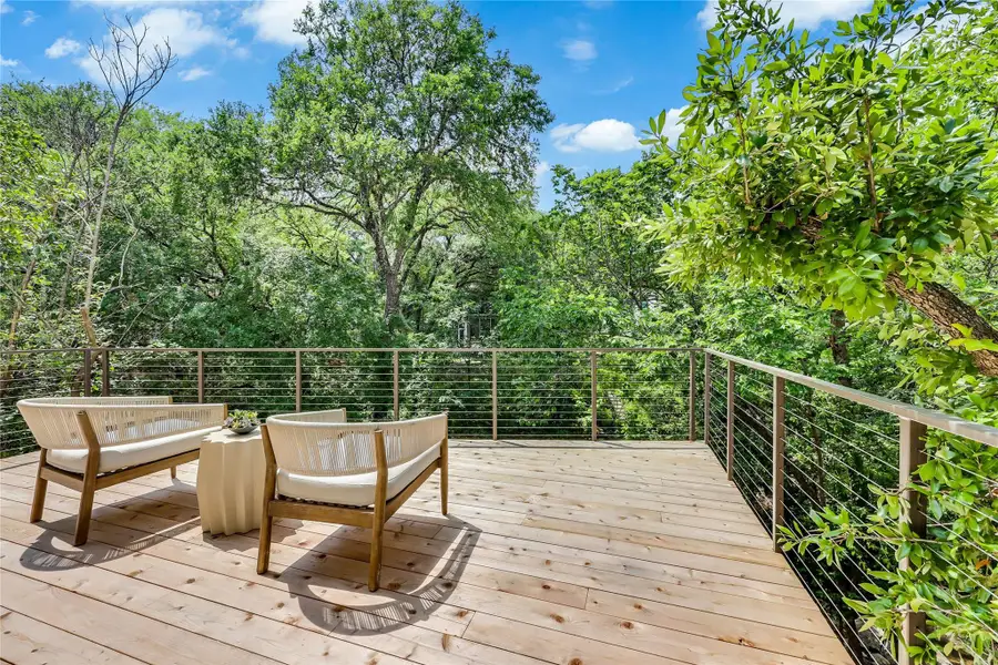Expansive outdoor deck featuring natural wood-finish flooring, contemporary cable railing, and surrounding mature foliage