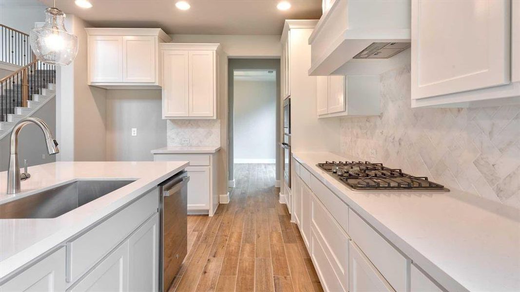 Kitchen featuring premium range hood, sink, white cabinetry, hanging light fixtures, and appliances with stainless steel finishes