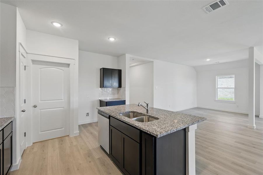 Kitchen featuring light stone counters, backsplash, visible vents, dishwasher, and a sink Kitchen featuring light stone counters, backsplash, visible vents, dishwasher, and a sink