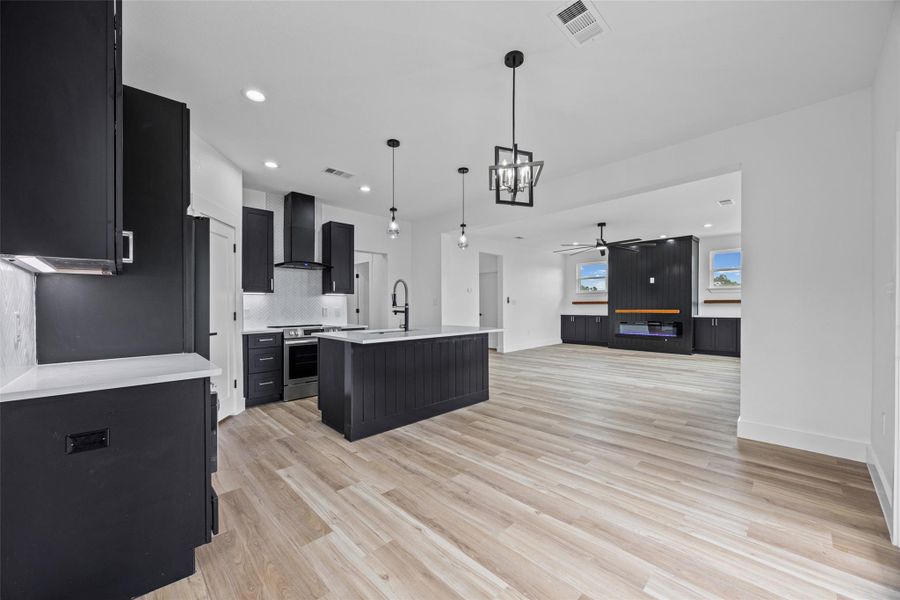 Modern kitchen featuring black cabinetry, a central island with sink, stainless steel appliances, light-toned wood-finish flooring, and recessed lighting Modern kitchen featuring black cabinetry, a central island with sink, stainless steel appliances, light-toned wood-finish flooring, and recessed lighting