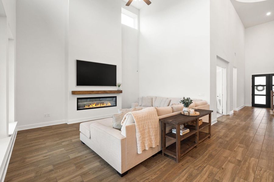 A spacious living room welcomes with soaring ceilings, rich wood flooring, and a modern linear fireplace.