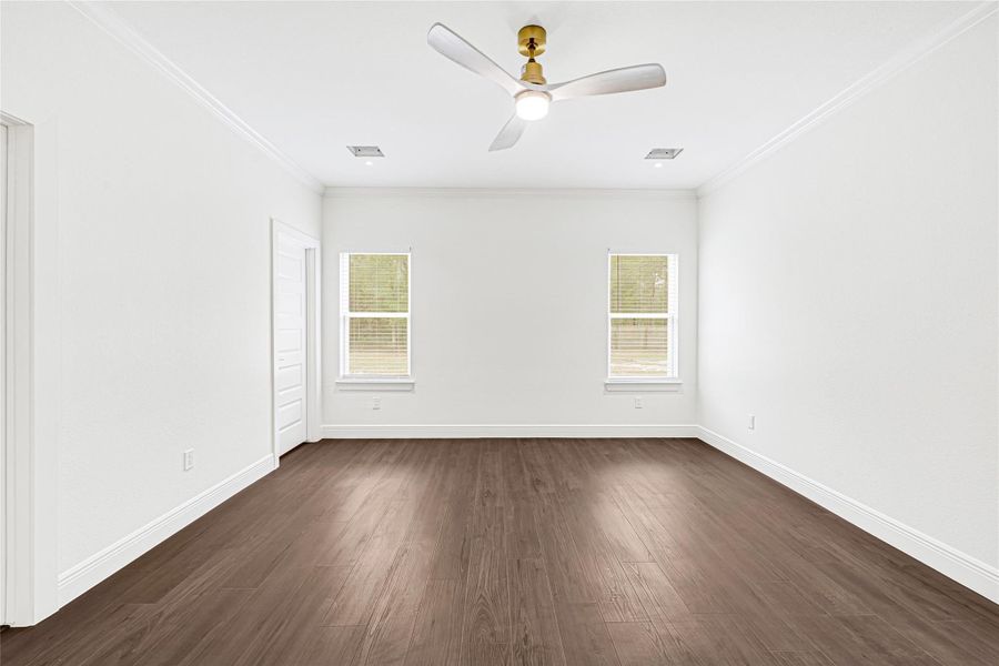Bright, spacious room with white walls and dark wood flooring. Features a modern ceiling fan, two windows for natural light, and a door leading to an adjacent space. Bright, spacious room with white walls and dark wood flooring. Features a modern ceiling fan, two windows for natural light, and a door leading to an adjacent space.