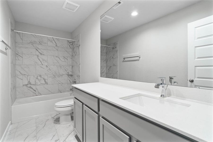 Secondary bath features tile flooring, bath/shower combo with tile surround, stained cabinets, beautiful light countertops, mirror, sleek fixtures and modern finishes.