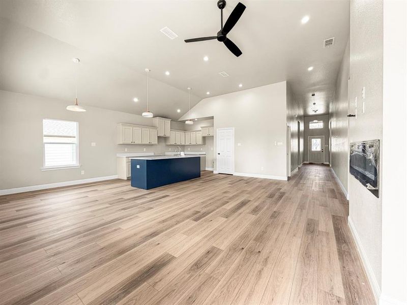 Unfurnished living room with a ceiling fan, healthy amount of natural light, light wood-type flooring, recessed lighting, and vaulted ceiling