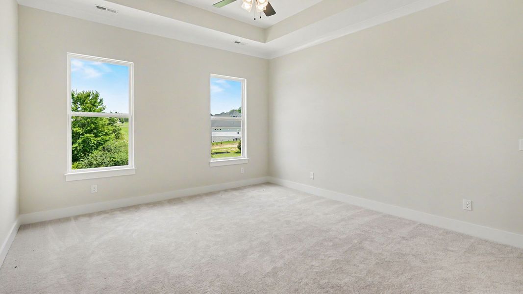 Primary suite with tray ceiling, ceiling fan, and carpet Primary suite with tray ceiling, ceiling fan, and carpet