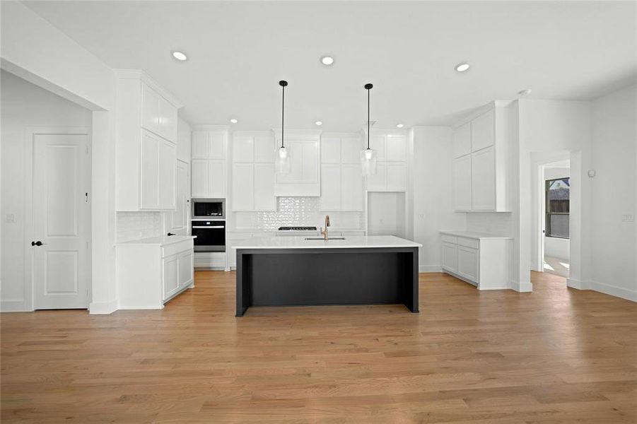 Kitchen featuring backsplash, white cabinetry, an island with sink, a breakfast bar, and recessed lighting Kitchen featuring backsplash, white cabinetry, an island with sink, a breakfast bar, and recessed lighting
