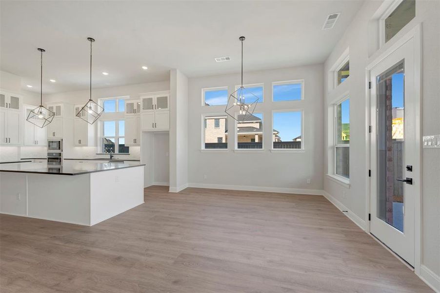 Kitchen featuring glass fronted cabinets, a chandelier, white cabinets, light wood finished floors, and a center island