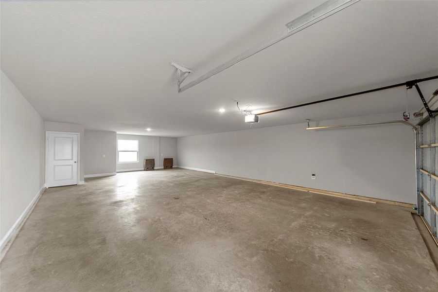 Spacious garage featuring a concrete floor, bright overhead lighting, and a white interior door