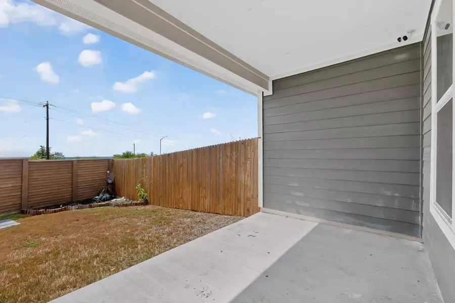 A covered concrete patio overlooks a fenced backyard under open blue skies. A covered concrete patio overlooks a fenced backyard under open blue skies.
