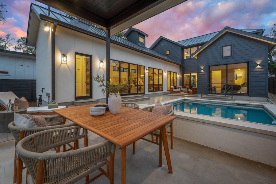 Back of property at dusk with a patio, outdoor dining space, an outdoor pool, a metal roof, and a standing seam roof