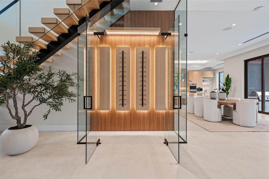 Striking glass-enclosed wine display with custom backlit wood paneling, floating staircase, and direct connection to the open dining and kitchen area. Striking glass-enclosed wine display with custom backlit wood paneling, floating staircase, and direct connection to the open dining and kitchen area.