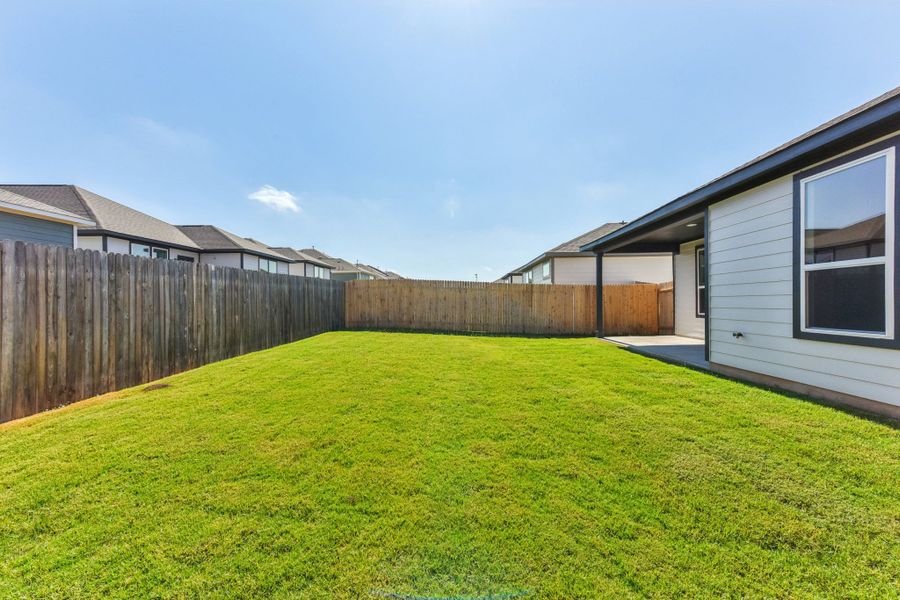 A fenced in yard with a house and a grass yard.