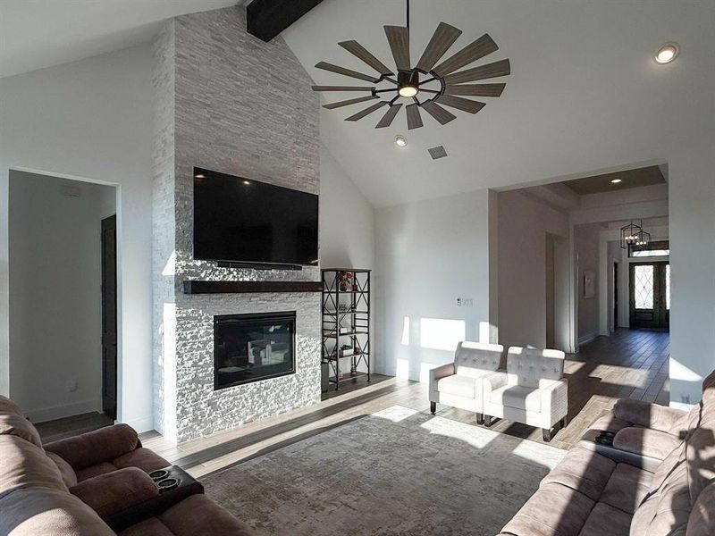 Living room with wood finished floors, high vaulted ceiling, beam ceiling, and a stone fireplace Living room with wood finished floors, high vaulted ceiling, beam ceiling, and a stone fireplace