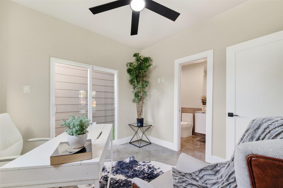 The first-floor bedroom is a versatile space suited equally to a guest suite, home office, or private retreat. Polished concrete floors, a ceiling fan, and an en-suite bath offer comfort and convenience, with natural light from street-facing windows and a glimpse of the full bath just off the room.