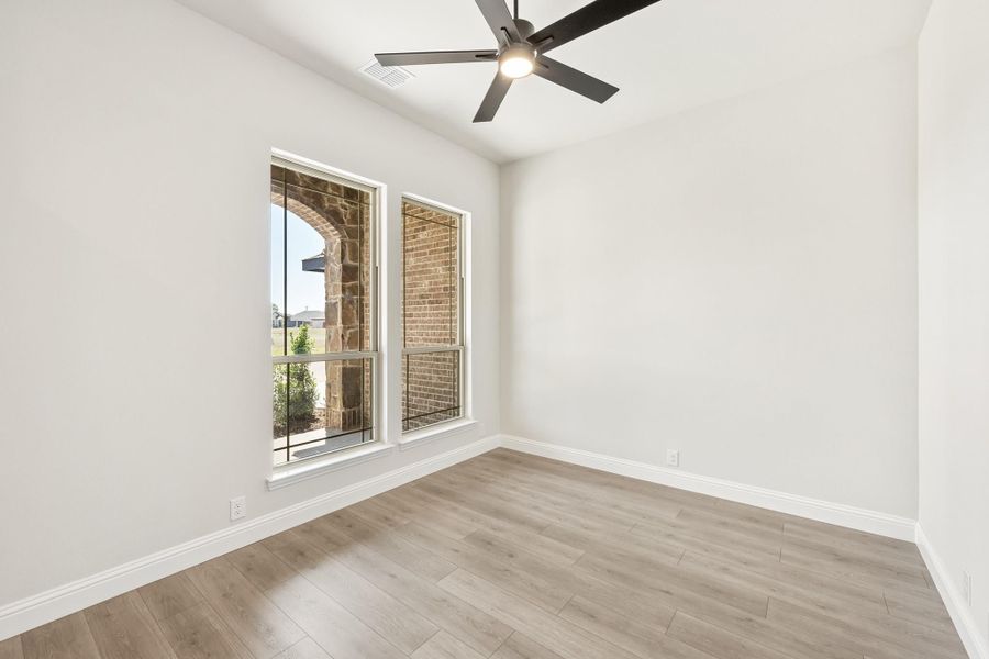 Empty room with light wood floors, white walls, ceiling fan, and two windows with brick exterior view Empty room with light wood floors, white walls, ceiling fan, and two windows with brick exterior view