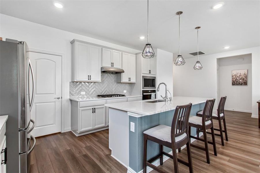 Kitchen featuring appliances with stainless steel finishes, under cabinet range hood, dark wood finished floors, light countertops, and tasteful backsplash