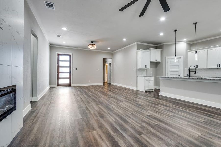 Unfurnished living room featuring a ceiling fan, crown molding, recessed lighting, dark wood-style flooring, and a premium fireplace Unfurnished living room featuring a ceiling fan, crown molding, recessed lighting, dark wood-style flooring, and a premium fireplace